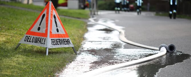 Eures • Feuerwehr im Einsatz, Warnschild und Wasserschlauch auf Straße.