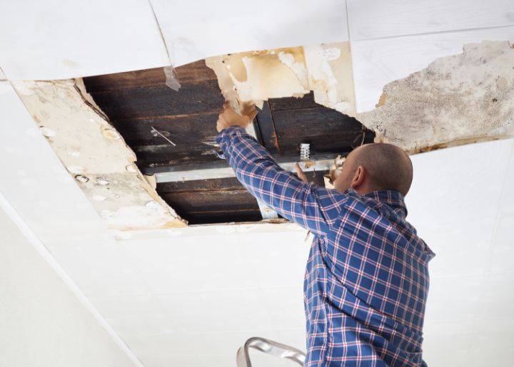 brand-wasserschaeden-start Eures • Mitarbeiter repariert beschädigte Decke in Wohnraum.