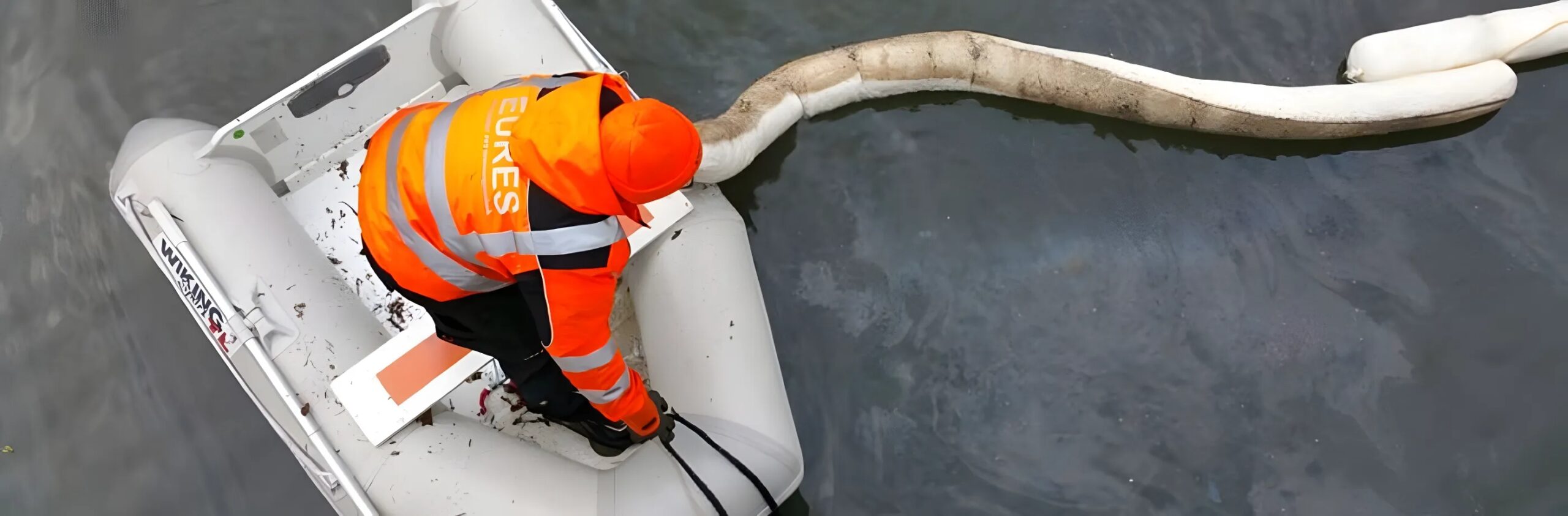 Eures • Mitarbeiter in orangefarbener Weste säubert Gewässer mit Boot.